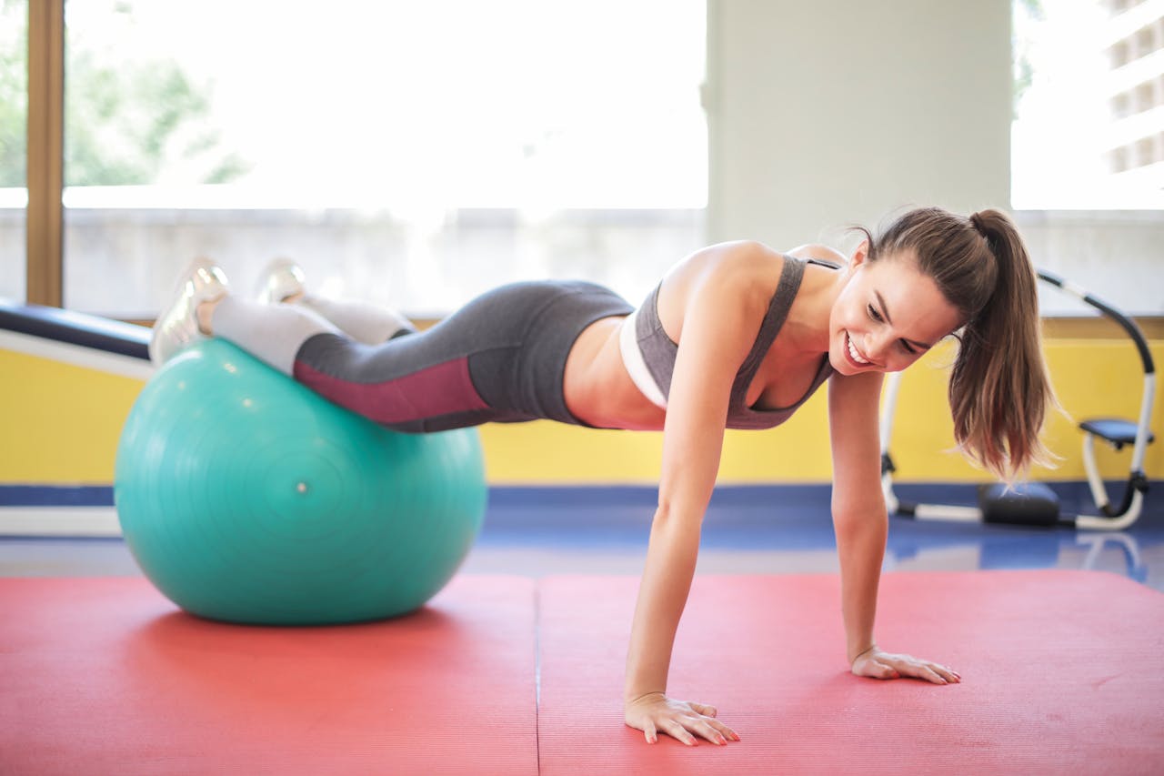 services-02 Active woman performing a workout with a stability ball indoors, showcasing fitness and strength.
