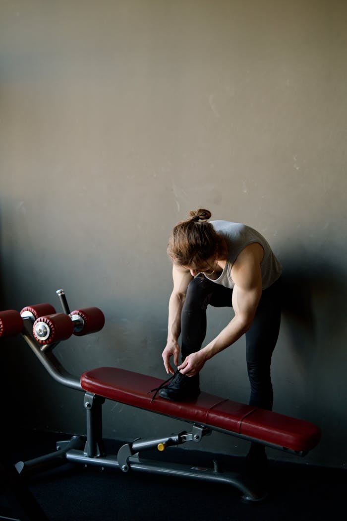 about-01 Muscular man preparing for workout, tying shoes in a modern gym environment.
